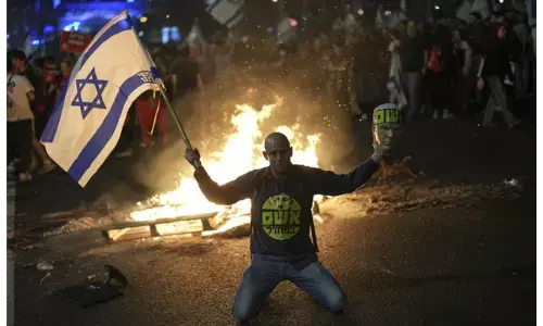 Photo of A protester holds an Israeli flag as Israelis light a bonfire during a protest after Prime Minister Benjamin Netanyahu has dismissed his defense minister Yoav Gallant in a surprise announcement in Tel Aviv, Israel, Tuesday, Nov. 5, 2024.